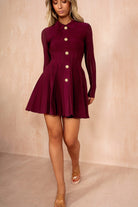 Woman wearing a burgundy dress with buttons against a beige background