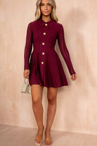 Woman wearing a burgundy dress with gold buttons against a beige background